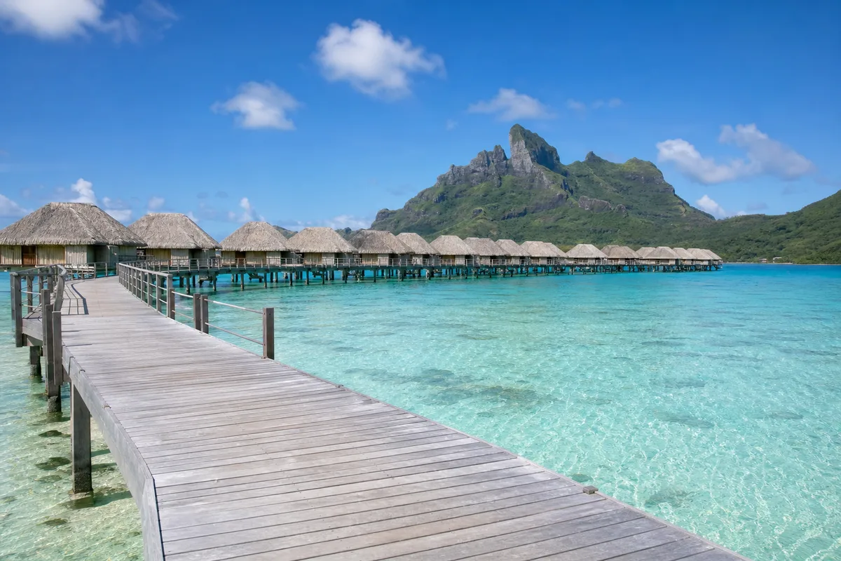 Bungalows sur pilotis au-dessus d&rsquo;un lagon turquoise en Polynésie, vus depuis un ponton en bois
